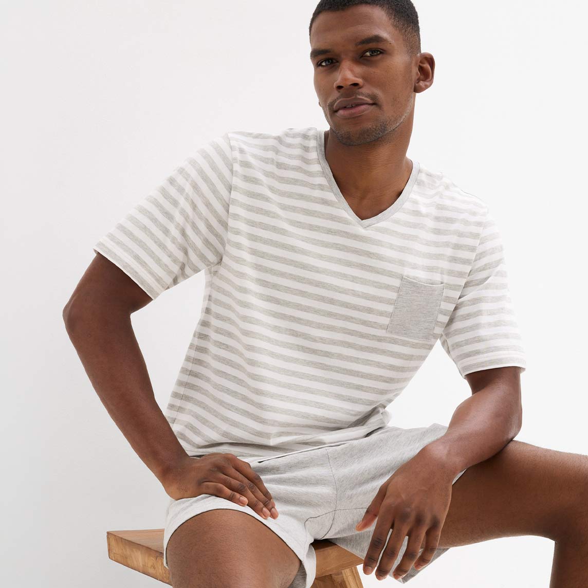 Gestreiftes V-Ausschnitt-T-Shirt in hellen Farbtönen, kombiniert mit einer kurzen, hellen Hose.