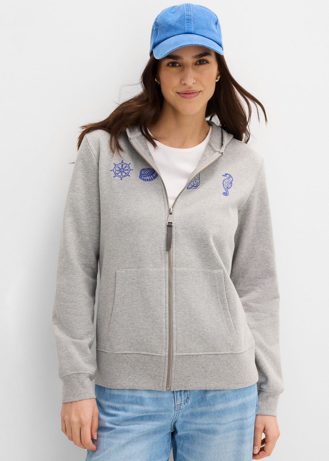 Grauer Hoodie mit maritimen Motiven, helle Jeans und blaue Kappe für einen sportlichen Look.