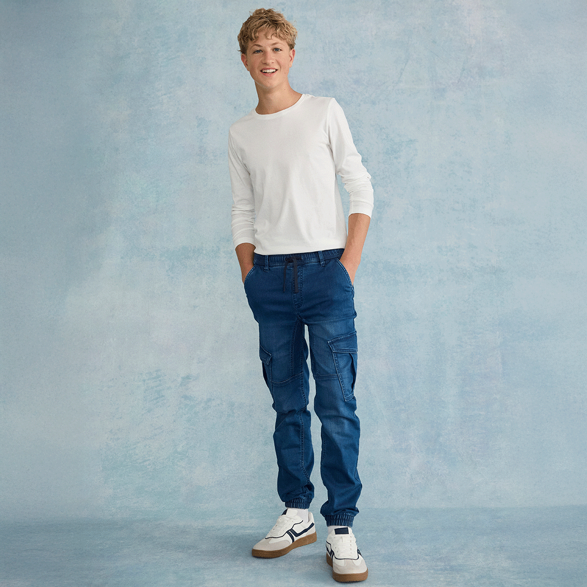 Lässiger Look: Weißer Pullover mit blauen Jeans und weißen Sneakers.