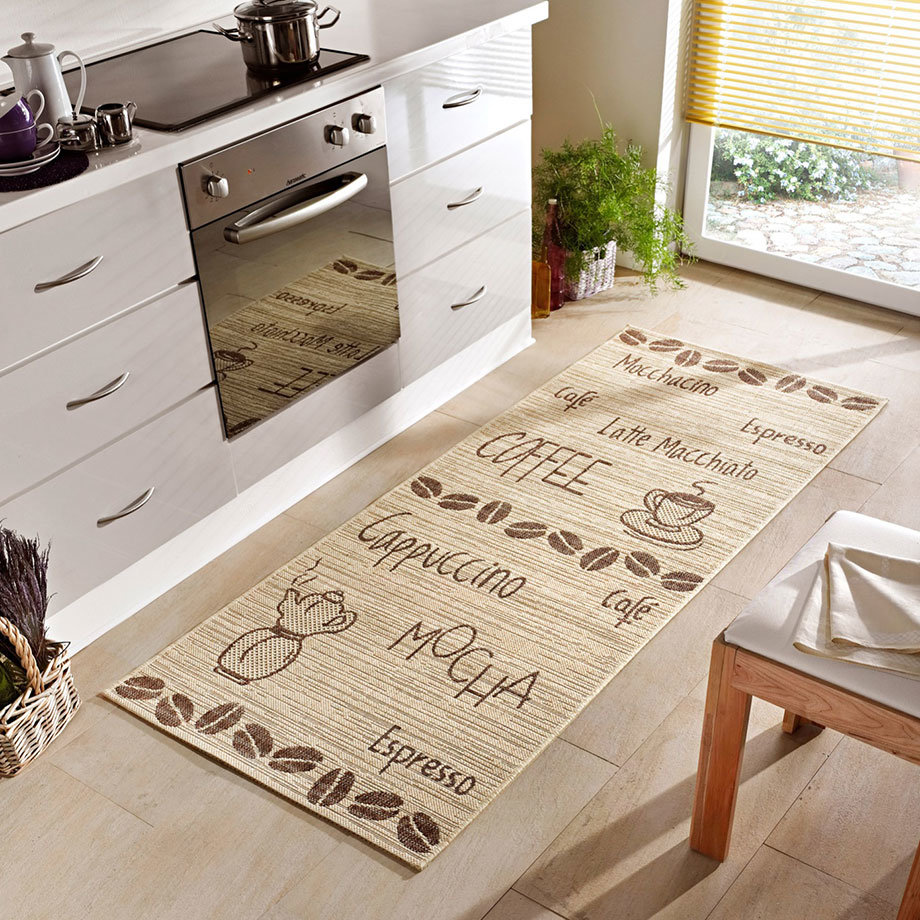 Ein beiger Küchenteppich mit Kaffee-Motiven liegt auf dem Boden vor weißen Küchenschränken.