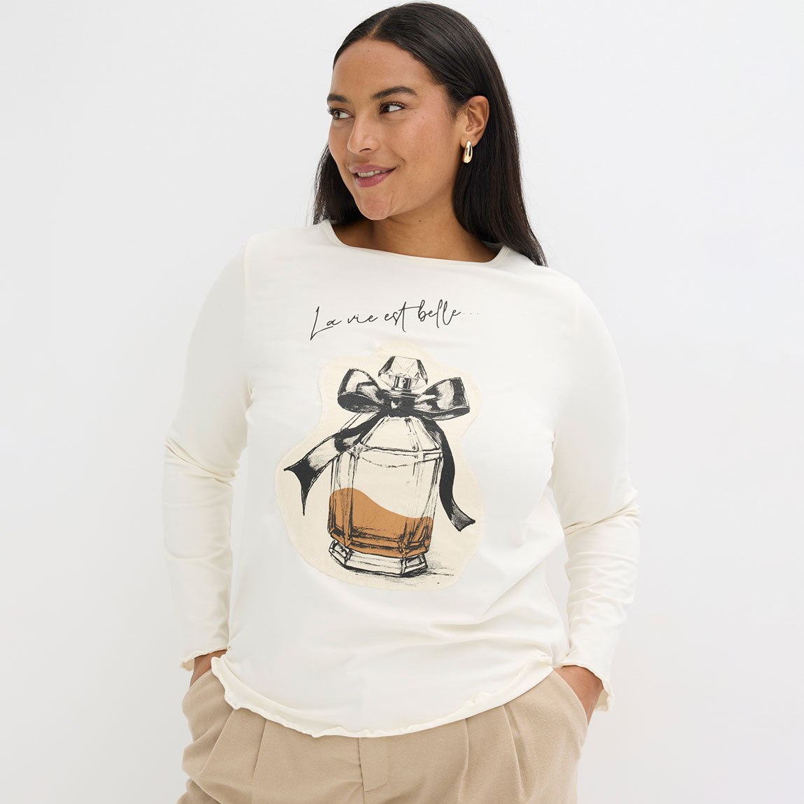 Ein cremefarbener Pullover mit Parfümflaschenmotiv und Schleife. 