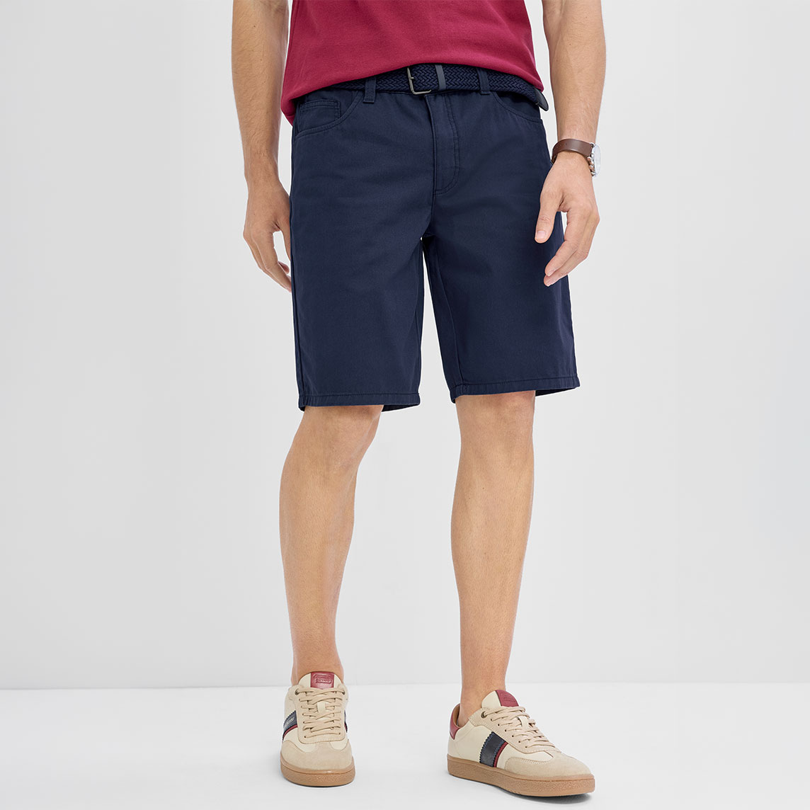 Sportlich: Rotes T-Shirt, marineblaue Shorts mit Gürtel und beige Sneaker.