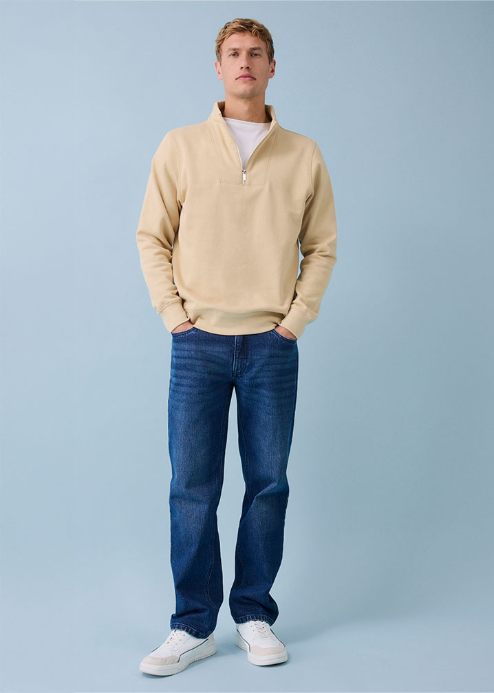 Beiger Pullover mit blauer Relaxed-Fit Jeans. 
