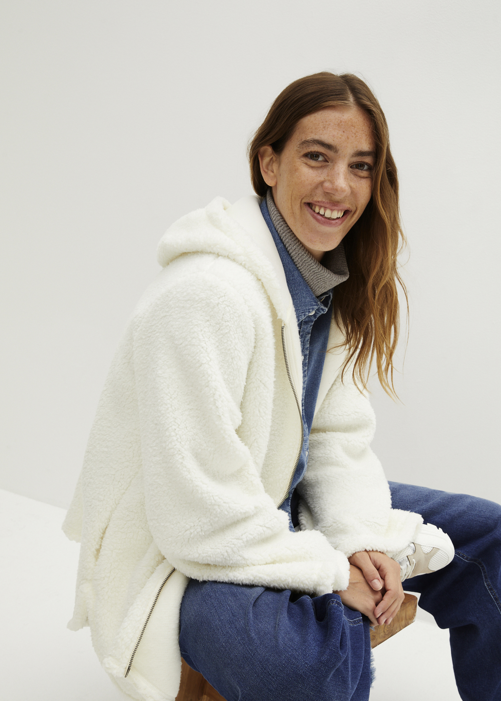 Weiße Teddyjacke über Denimhemd und Rollkragenpullover, dazu blaue Jeans.