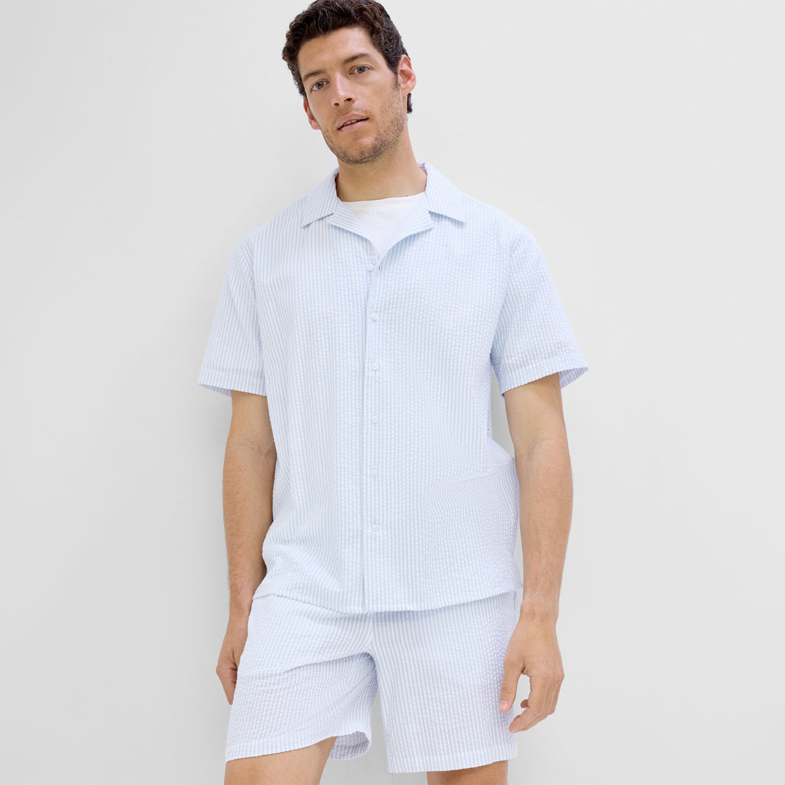 Mann trägt ein hellblau-weiß gestreiftes Kurzarmhemd mit passenden Shorts.