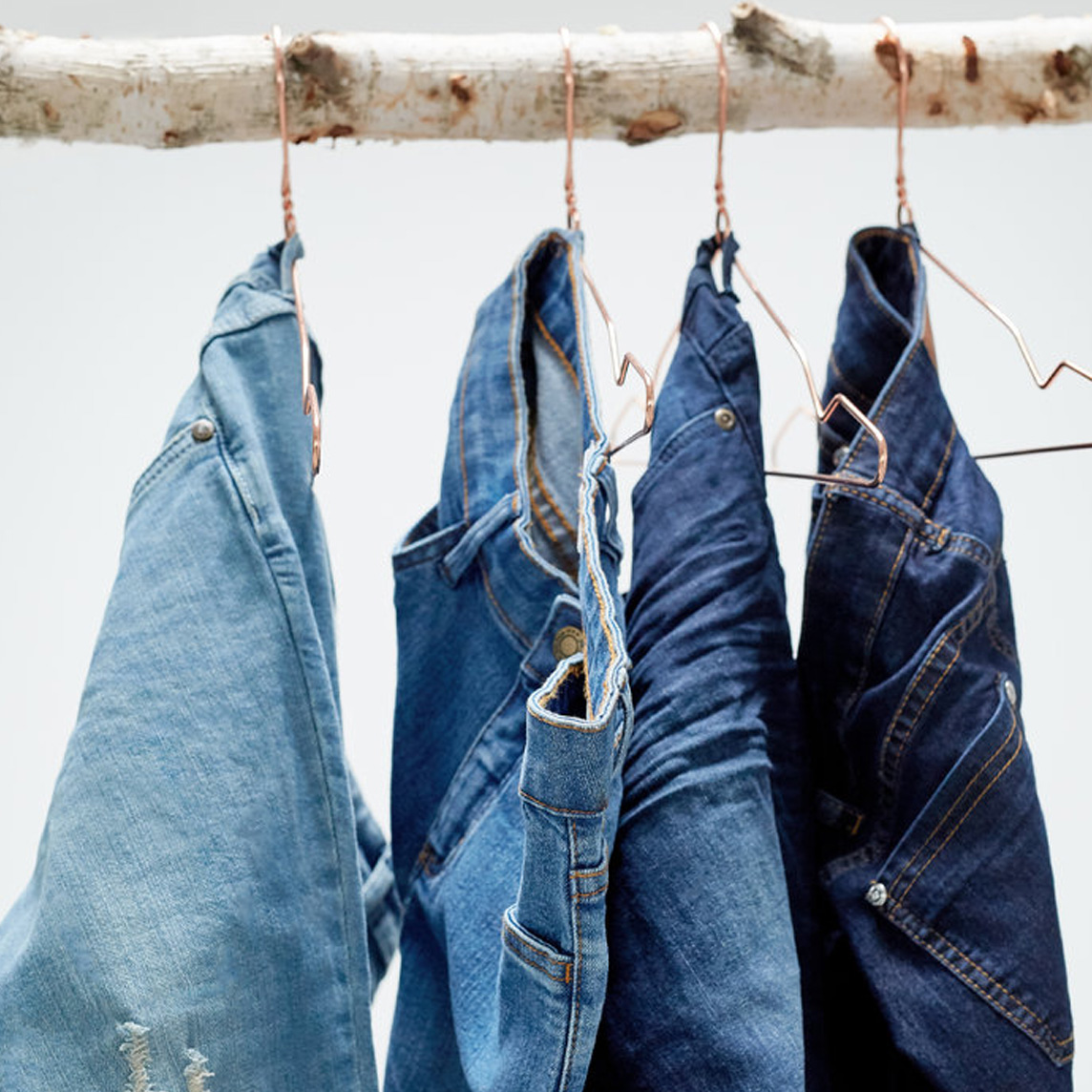 Eine Reihe blauer Jeans in verschiedenen Waschungen hängt ordentlich auf Kleiderbügeln.