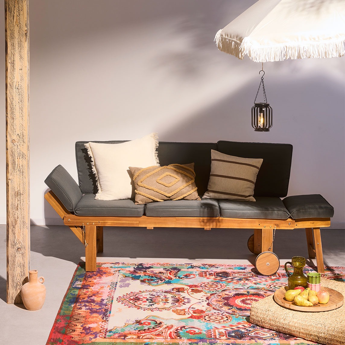 Gemütliche Terrasse mit Holzbank, weichen Kissen und buntem Teppich.