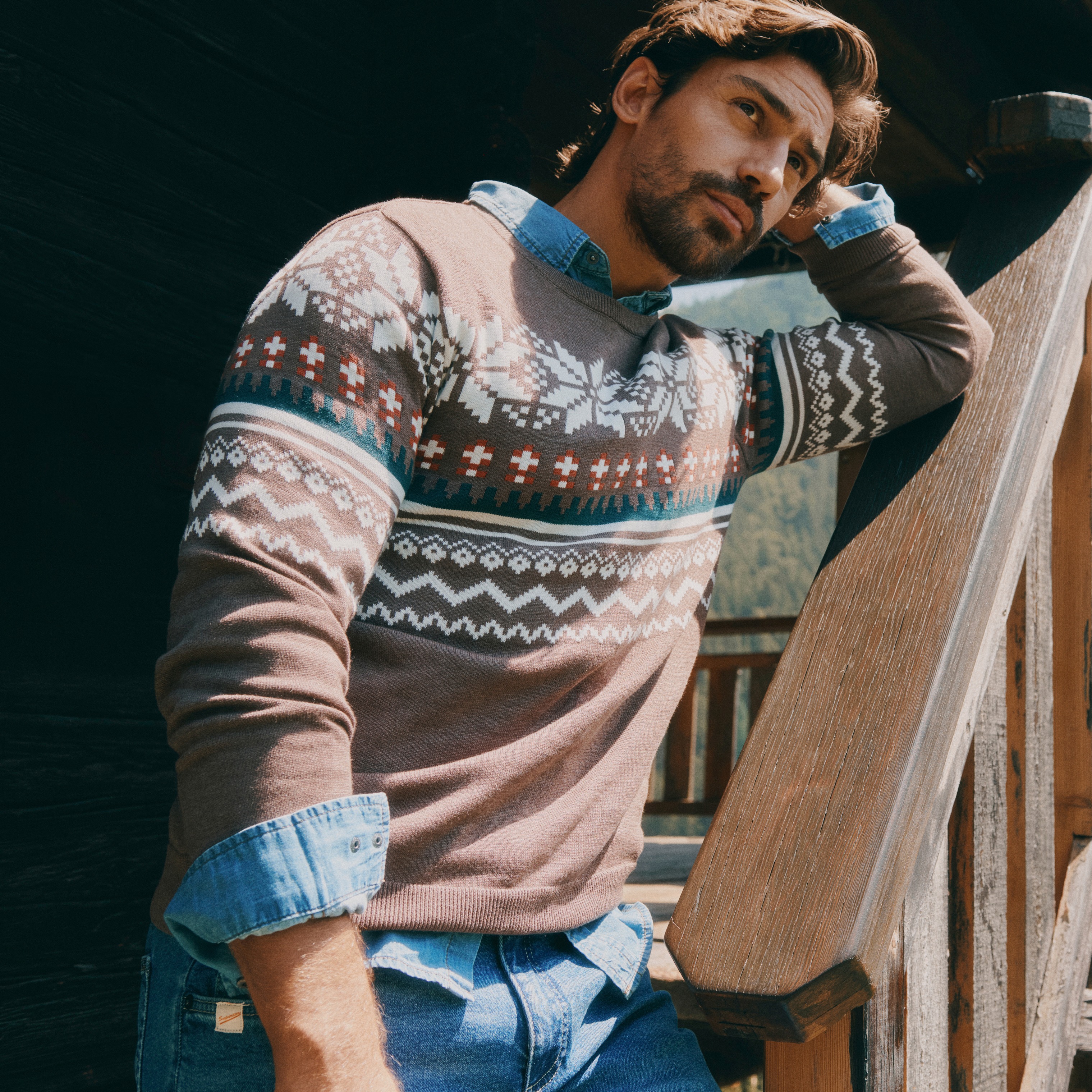 Der Mann trägt einen gemusterten Pullover über Jeanshemd und blauer Jeans.
