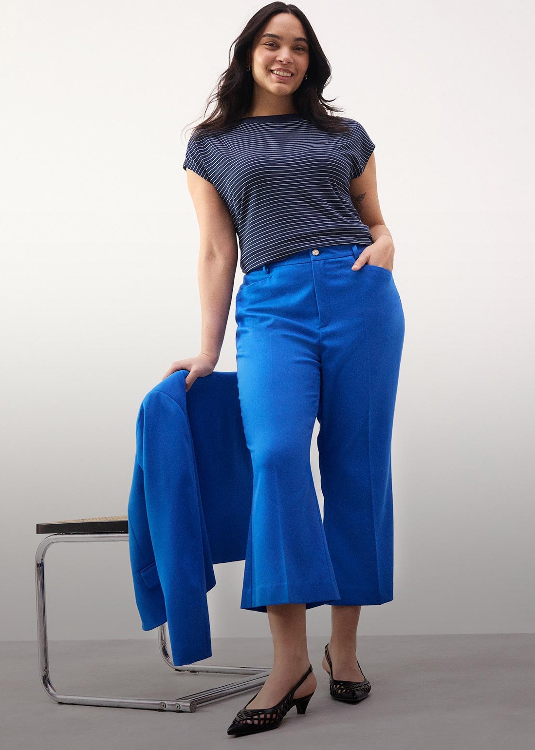 Eine strahlende Frau in einem schlichten weißen Kleid mit kurzen Ärmeln und Lochstickerei.