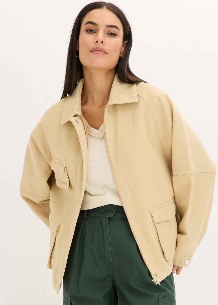 Lässige beige Jacke über hellem Top, kombiniert mit dunkelgrüner Hose.