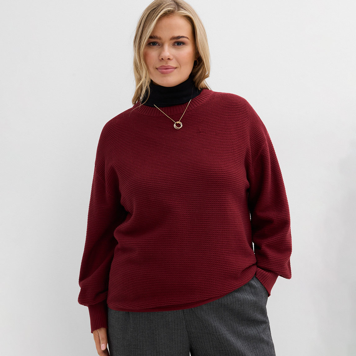 Roter Pullover kombiniert mit grauer Hose.