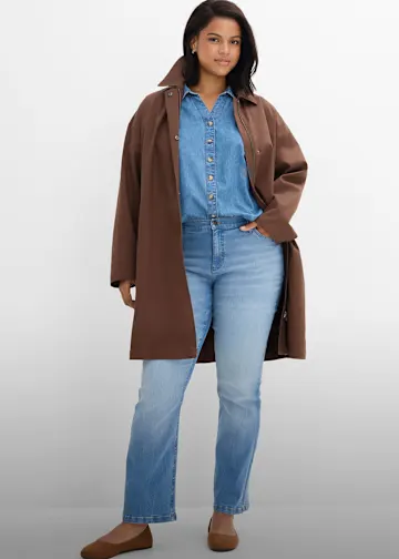 Brauner Mantel über Jeanshemd, helle Jeans und bequeme braune Schuhe.