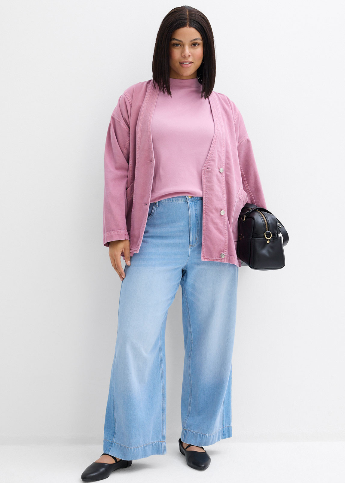 Rosafarbene Strickjacke über pastellrosa Top, kombiniert mit hellblauen Jeans und schwarzen Schuhen.