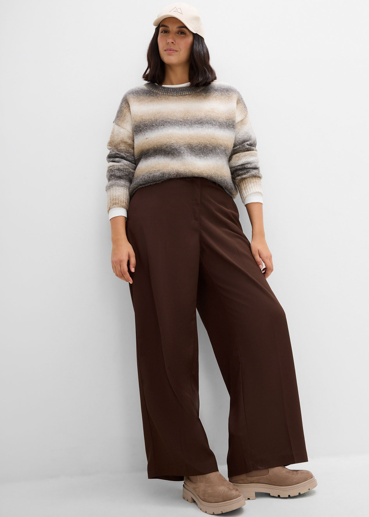 Gestreifter Pullover, braune weite Hose, bequeme Plateauschuhe und eine Kappe.
