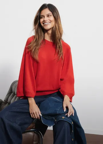 Roter Oversize-Pullover kombiniert mit weiten, blauen Denim-Hosen. Modisch und bequem.