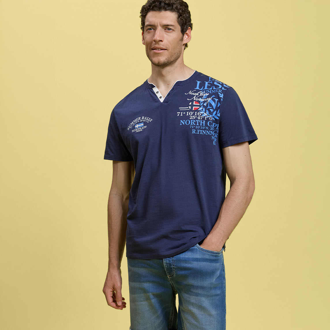 Er trägt ein lässiges, dunkelblaues Henley-Shirt mit auffälligem Print und helle Jeans.