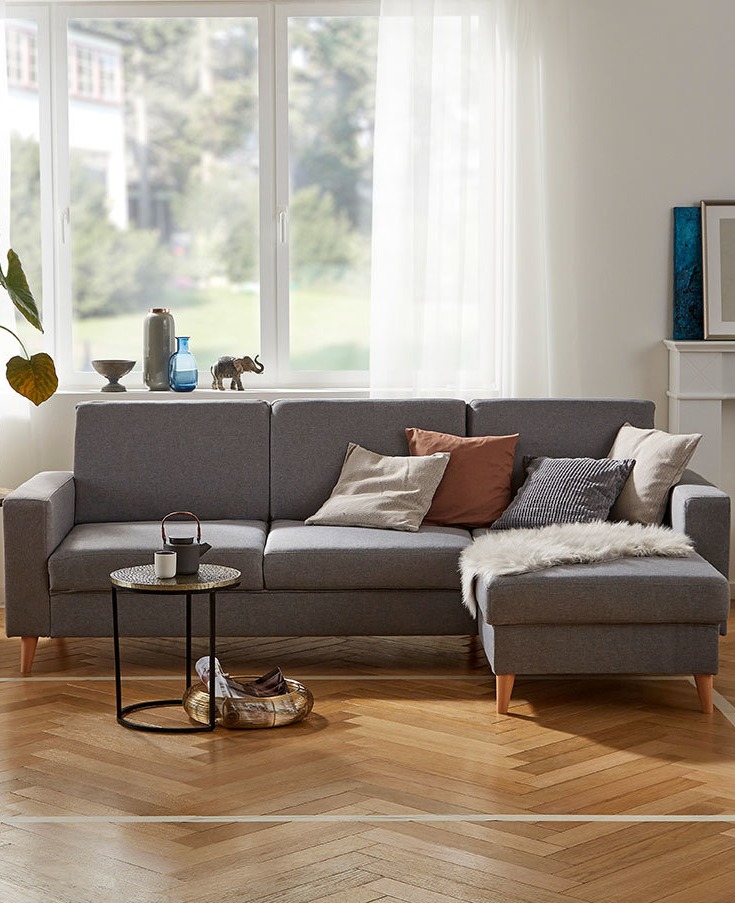 Graues Ecksofa mit Kissen in Erdtönen, gemütlich und einladend im hellen Wohnzimmer.