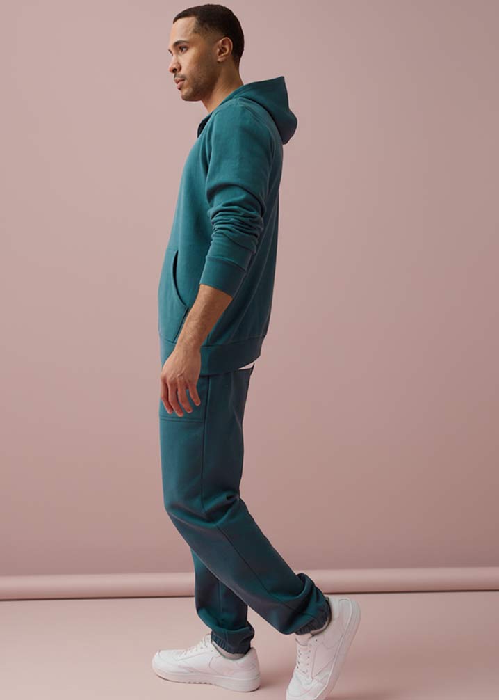 Türkisfarbener Trainingsanzug mit Reißverschluss und weiße Sneakers.