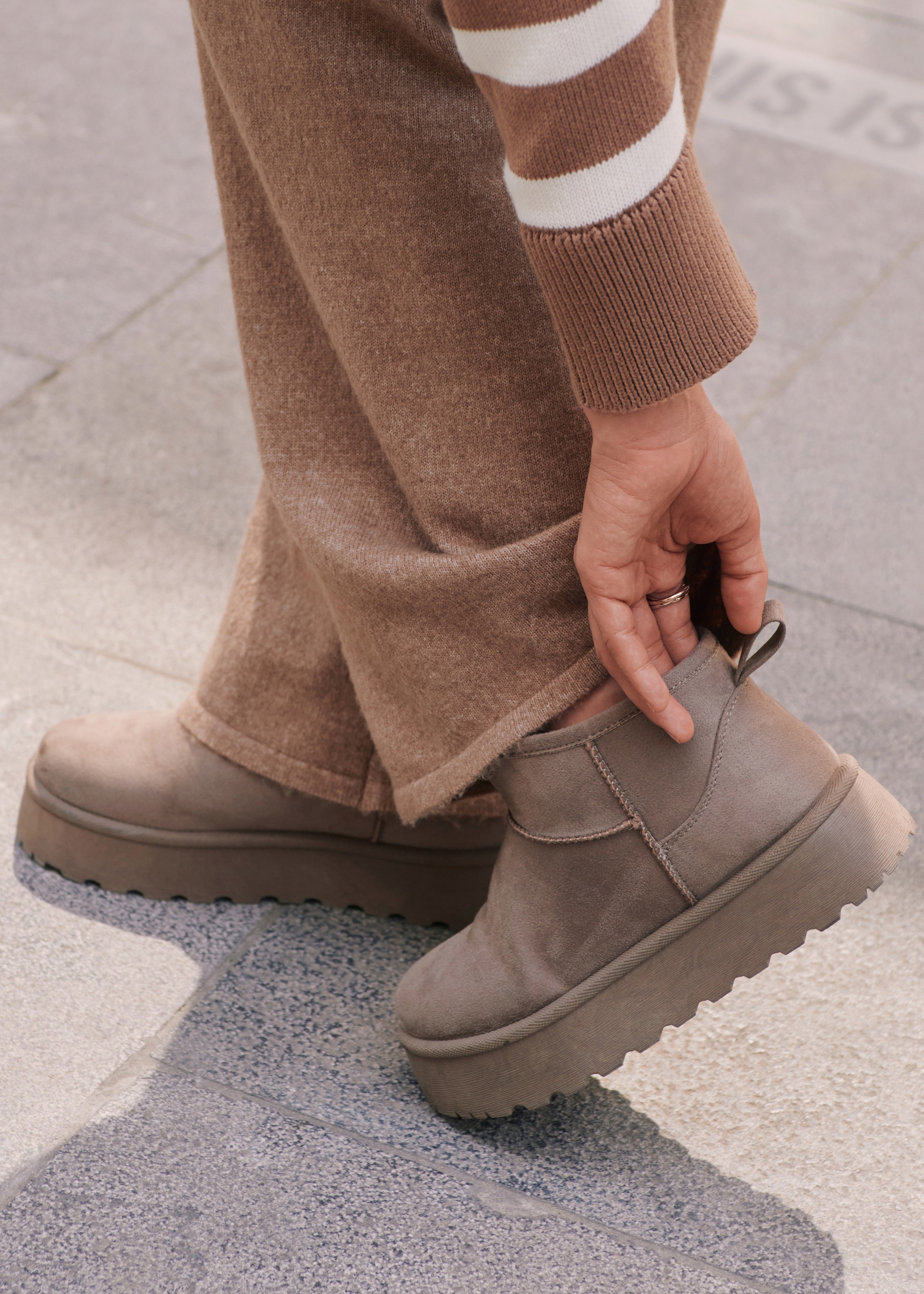 Brauner Pullover, weite Hose und graue Plateaustiefel prägen den komfortablen Look.