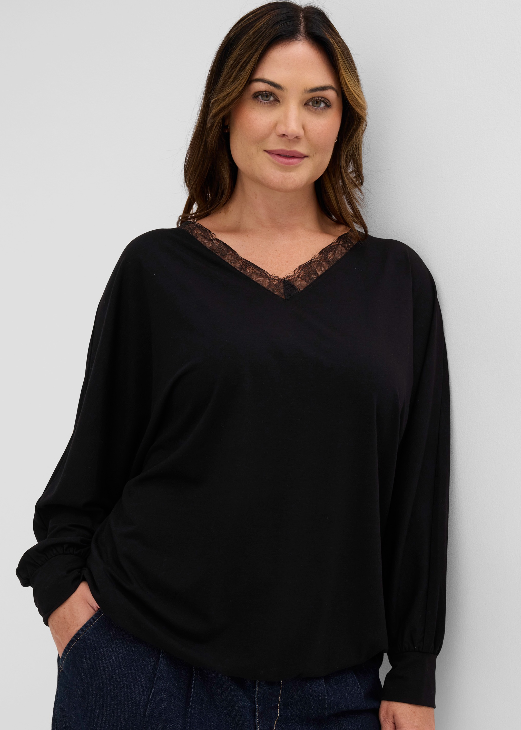 Modernes schwarzes Longsleeve mit zarter Spitze am V-Ausschnitt, dazu dunkle Jeans.