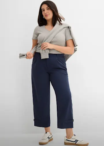 Graues Shirt, marineblaue Hose mit Bündchen, Pullover, weiße Sneaker.