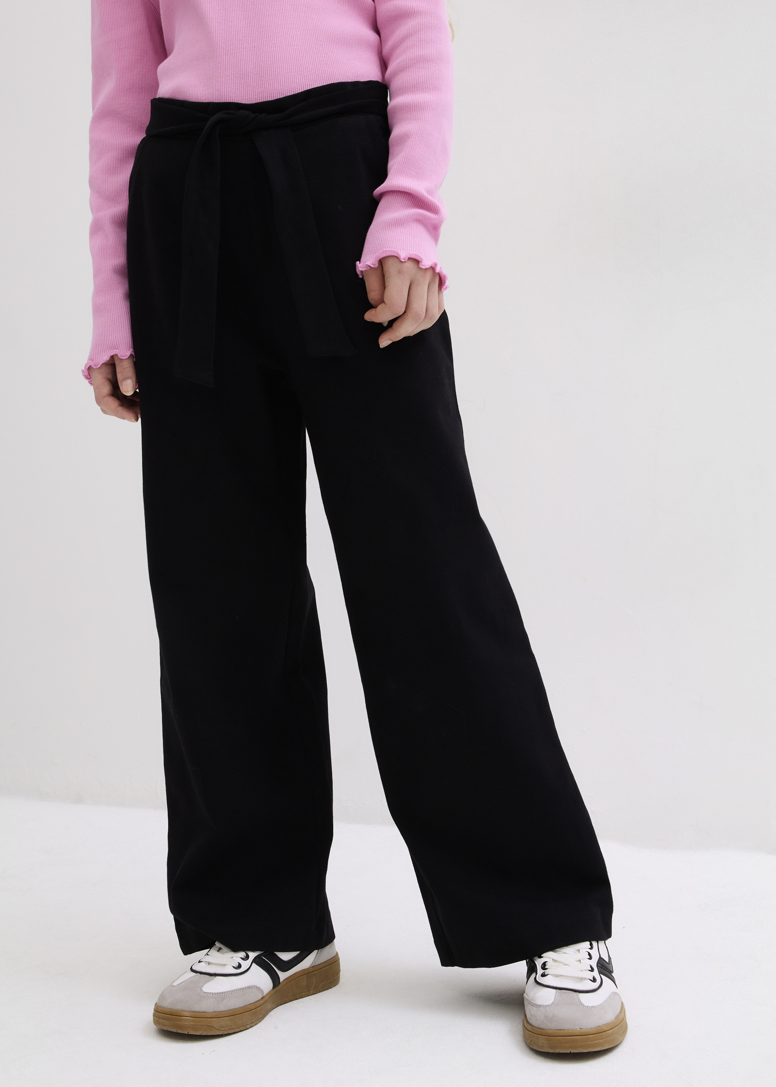 Rosafarbenes Oberteil, schwarze weite Hose mit Bindeband und sportliche Sneaker.