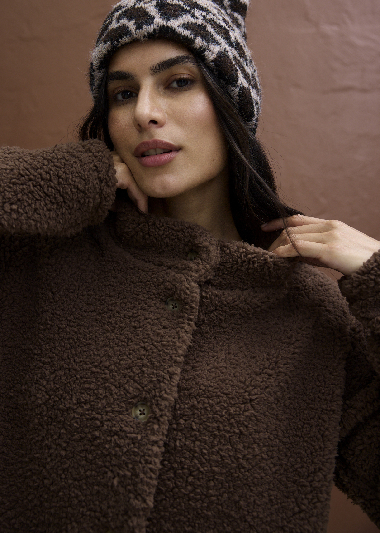 Eine kuschelige braune Teddyfelljacke und eine gemusterte Strickmütze prägen diesen warmen Look.