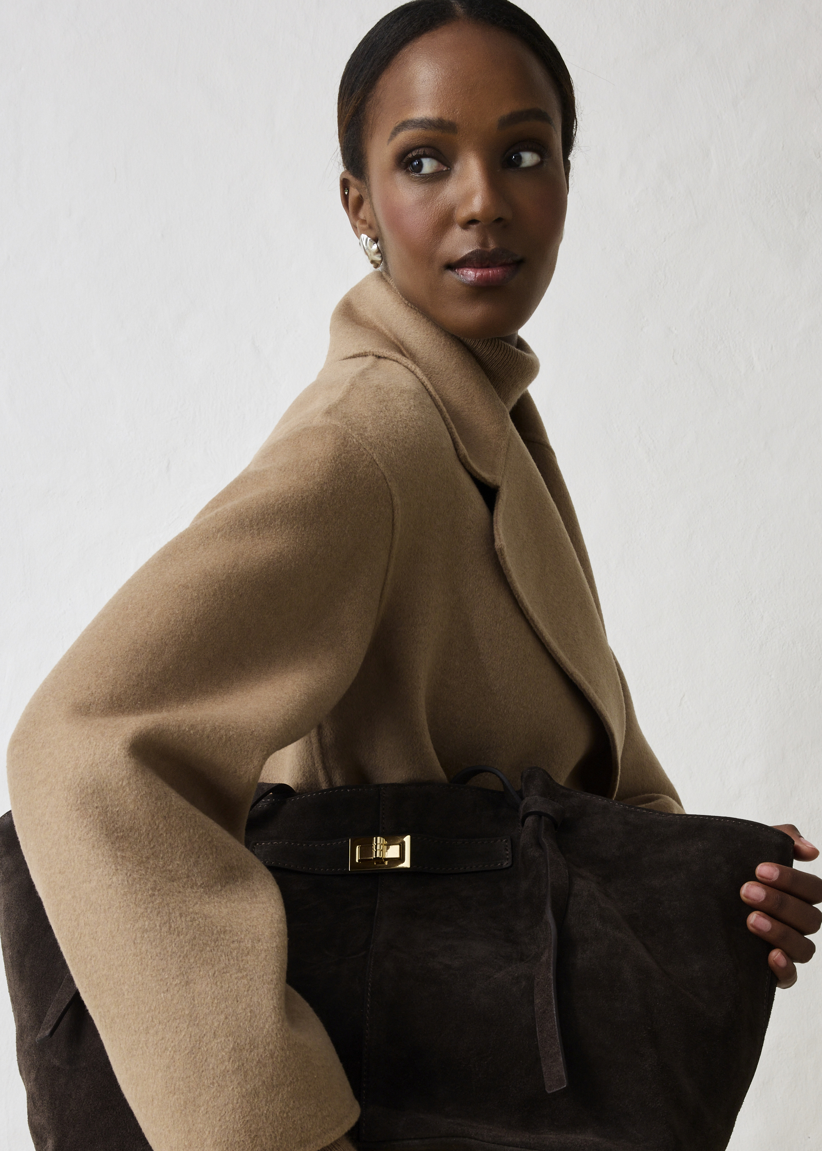 Warmer Kamel-Mantel über Rollkragenpullover, kombiniert mit einer großen Wildledertasche.