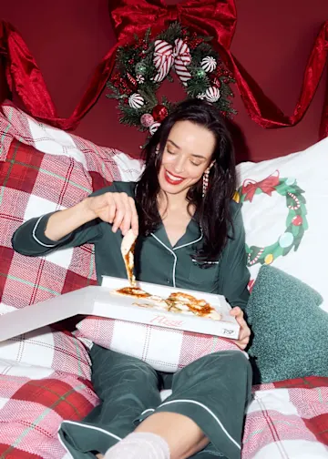 In einem gemütlichen dunkelgrünen Schlafanzug genießt sie Pizza im Bett.