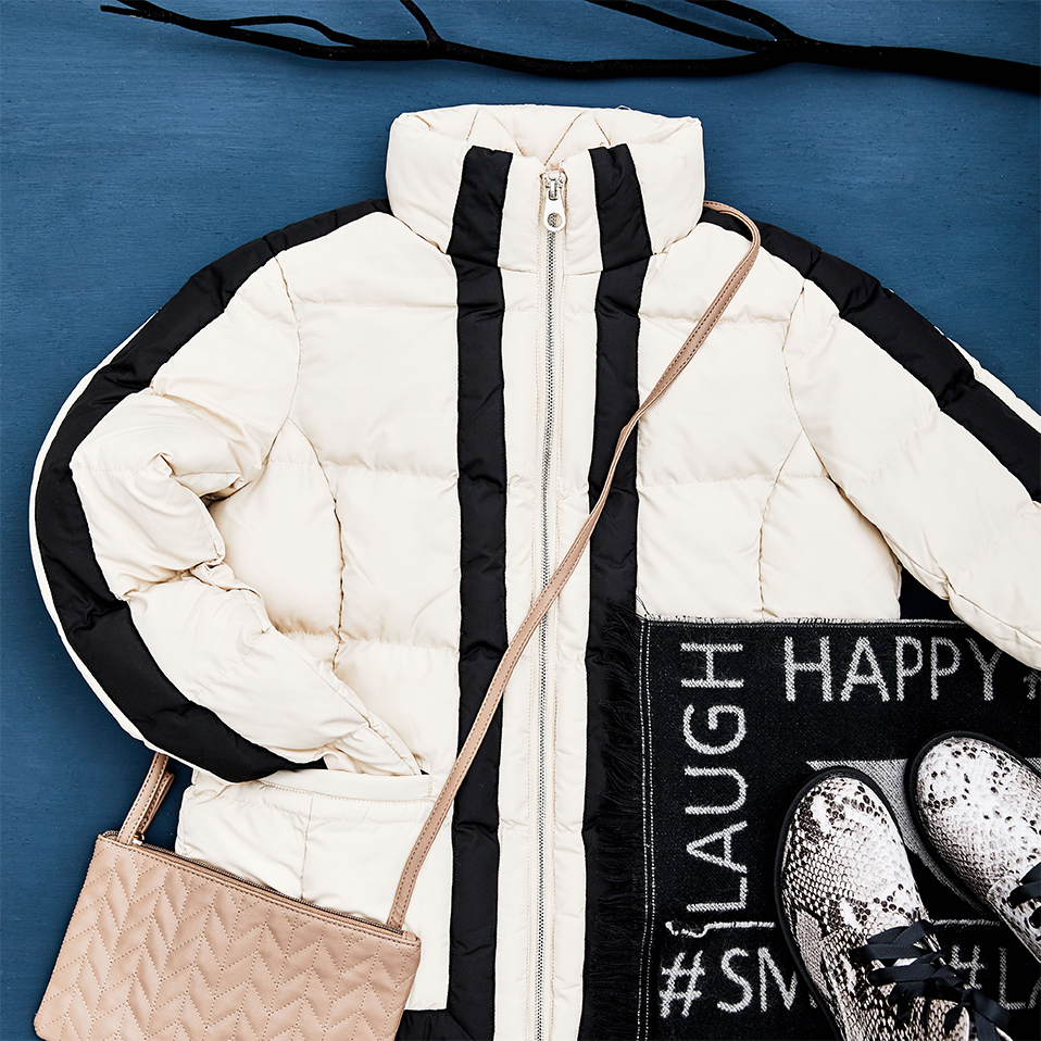 Weiße Winterjacke mit schwarzen Akzenten, gesteppte Handtasche und moderne Sneakers für einen stylischen Look.