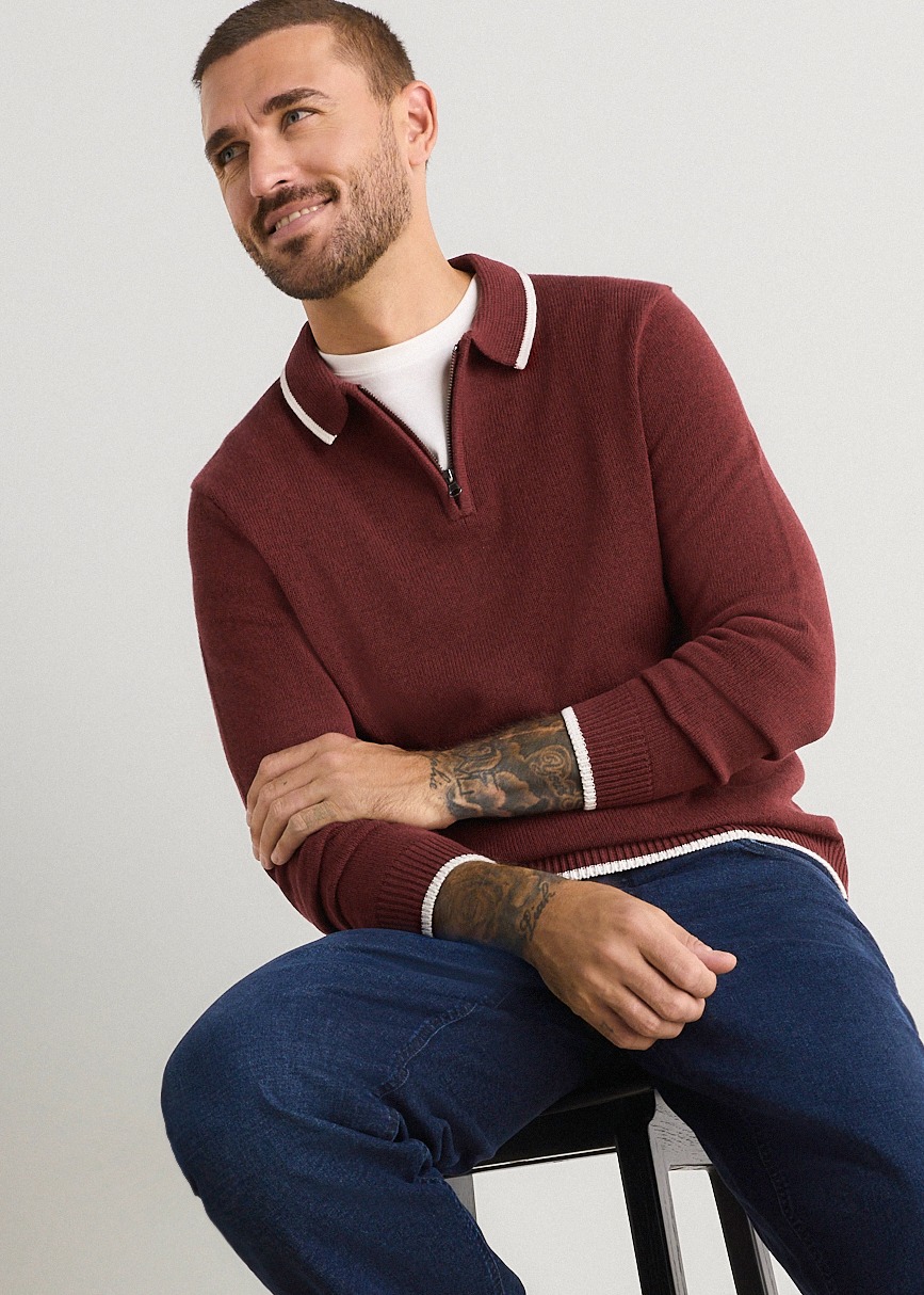 Weinroter Reißverschluss-Pullover mit weißen Akzenten, kombiniert mit blauen Jeans.