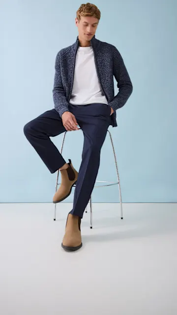 Dunkelblaue Strickjacke über weißem T-Shirt, dazu elegante Hose und beige Wildleder-Boots.