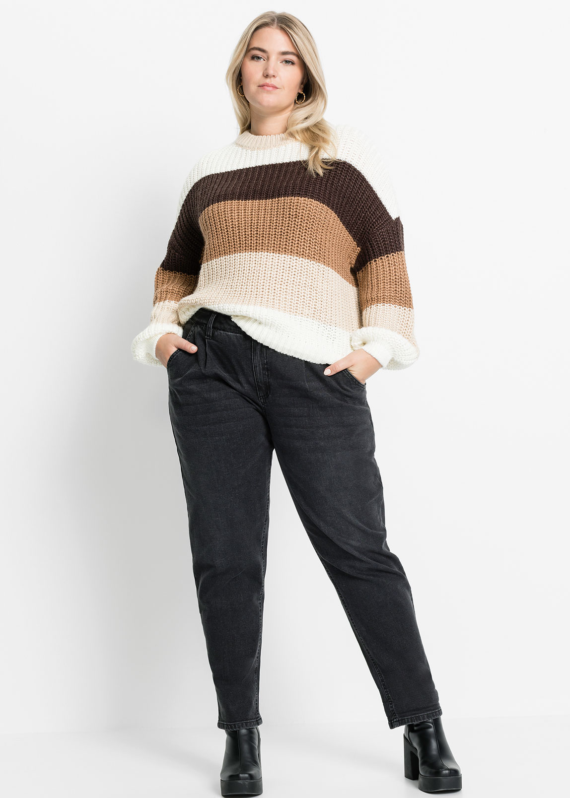 Gestreifter Strickpullover in Erdtönen, kombiniert mit dunkler Jeans und schwarzen Schuhen.