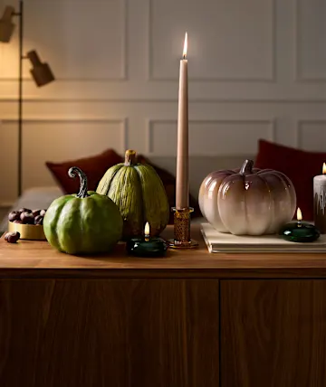 Gemütliche Herbstdekoration mit Kerzenlicht, kunstvollen Kürbissen und Kastanien auf Holz.