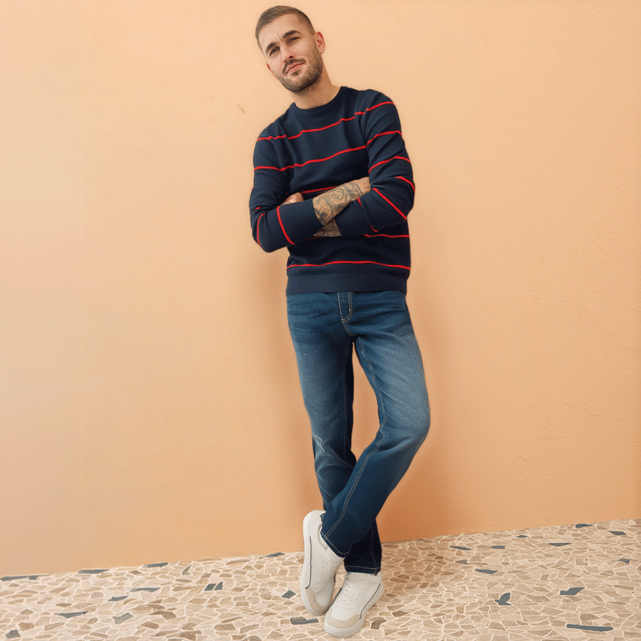 Gestreifter Pullover in dunklen Farben, blaue Jeans und weiße Sneaker bilden einen lässigen Look.