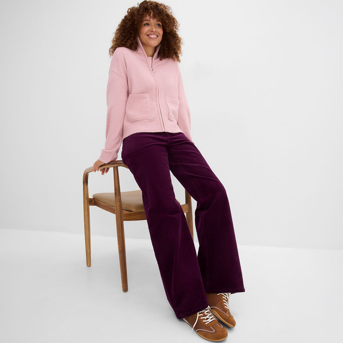 Rosa Sweatjacke, weite lila Cordhose und braune Schuhe.