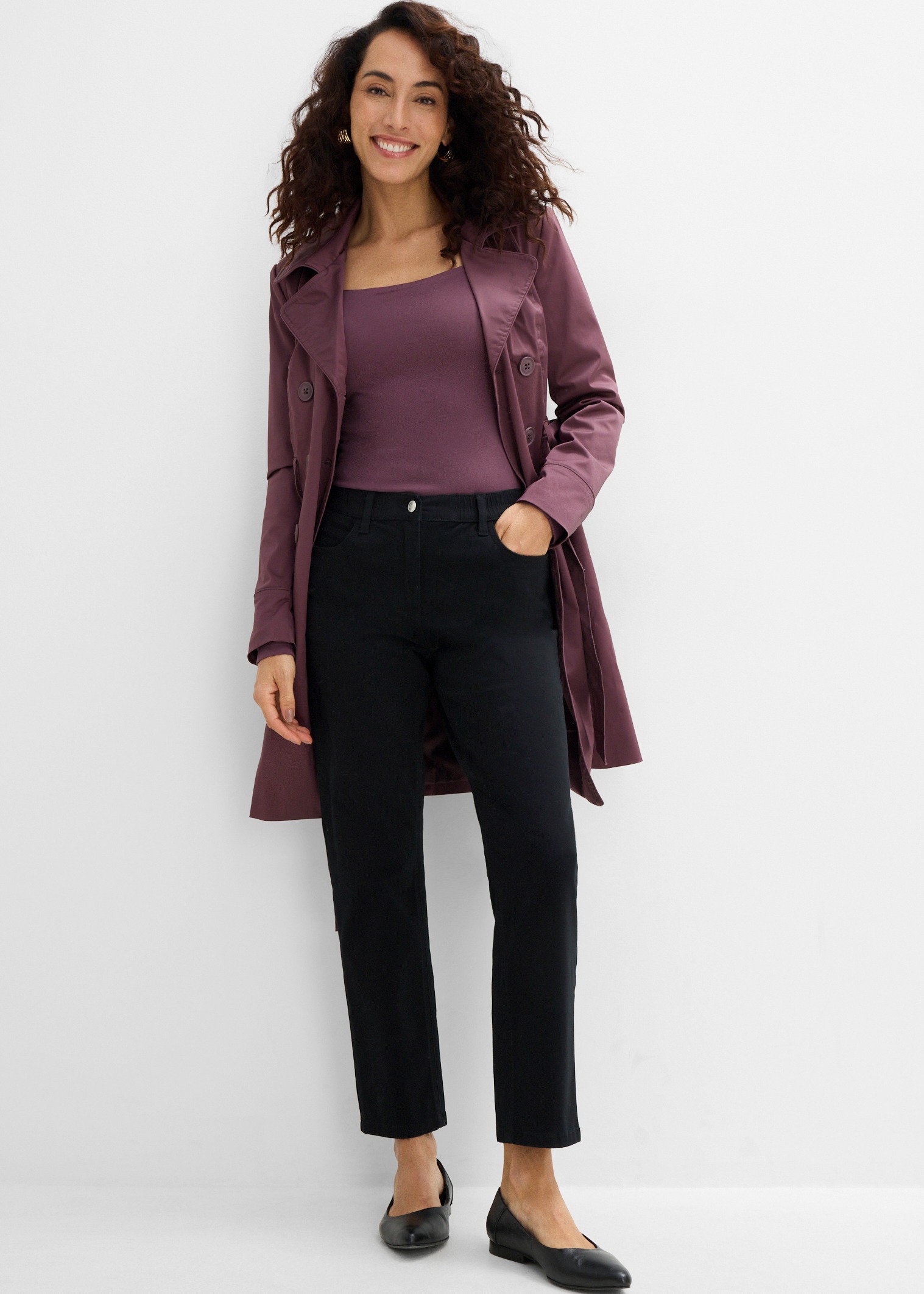 Eleganter mauvefarbener Trenchcoat, passendes Oberteil, schwarze Hose und schicke Ballerinas.