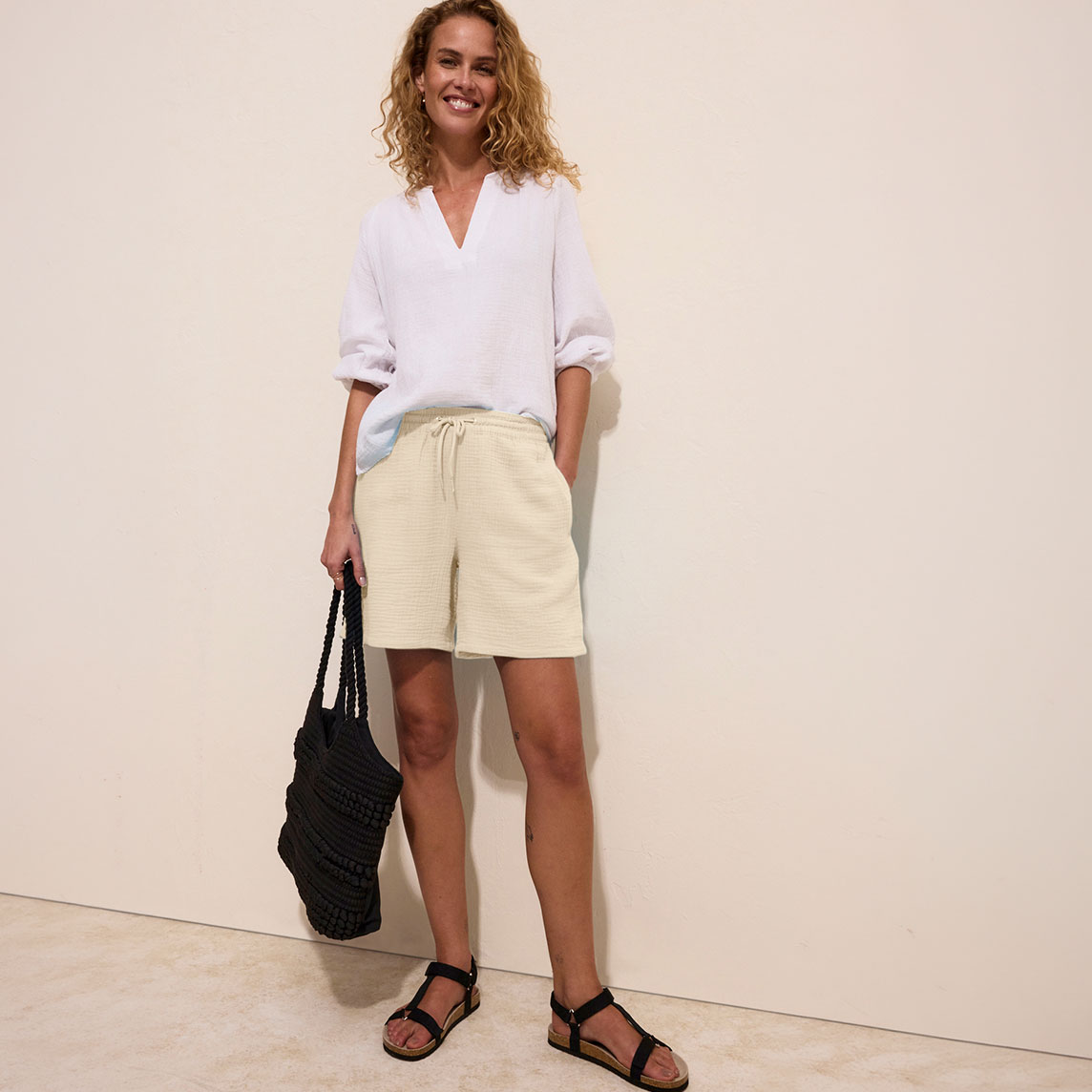 Weiße Bluse, beige Musselin-Shorts und schwarze Sandalen für einen lässigen Sommerlook.