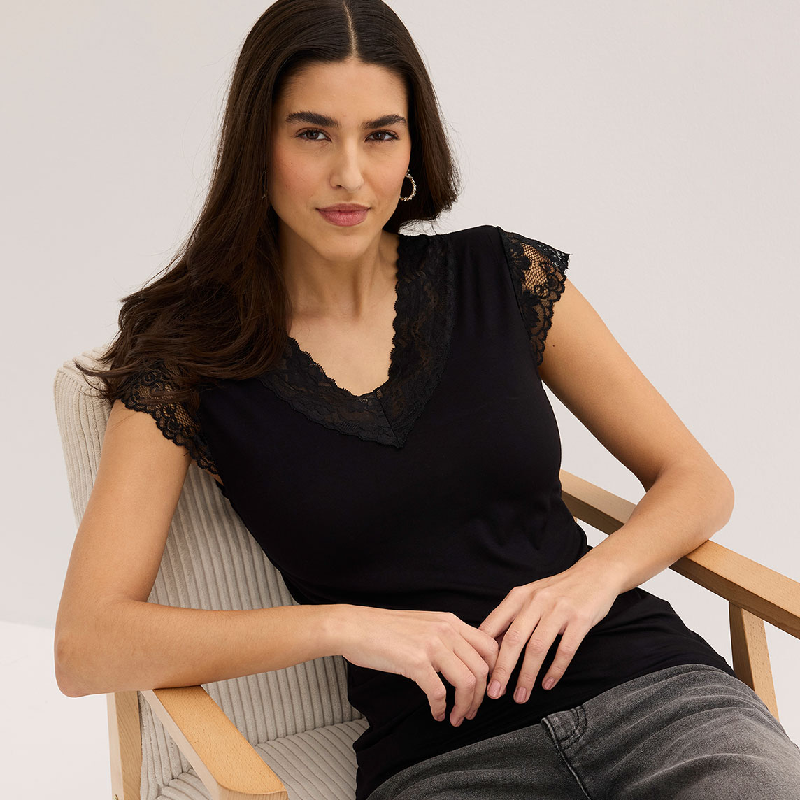 Elegantes schwarzes Top mit Spitzenbesatz am Ausschnitt, kombiniert mit lässigen Jeans.