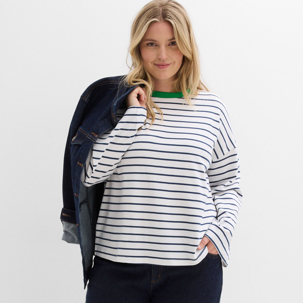 Gestreiftes Shirt mit grünem Kragen, dunkelblaue Jeansjacke über die Schulter geworfen.