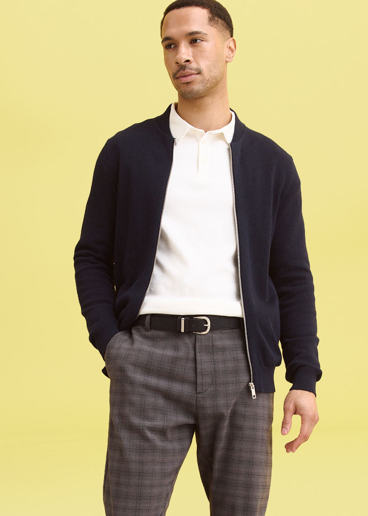 Schwarze Strickjacke über weißem T-Shirt kombiniert mit grau karierter Hose.