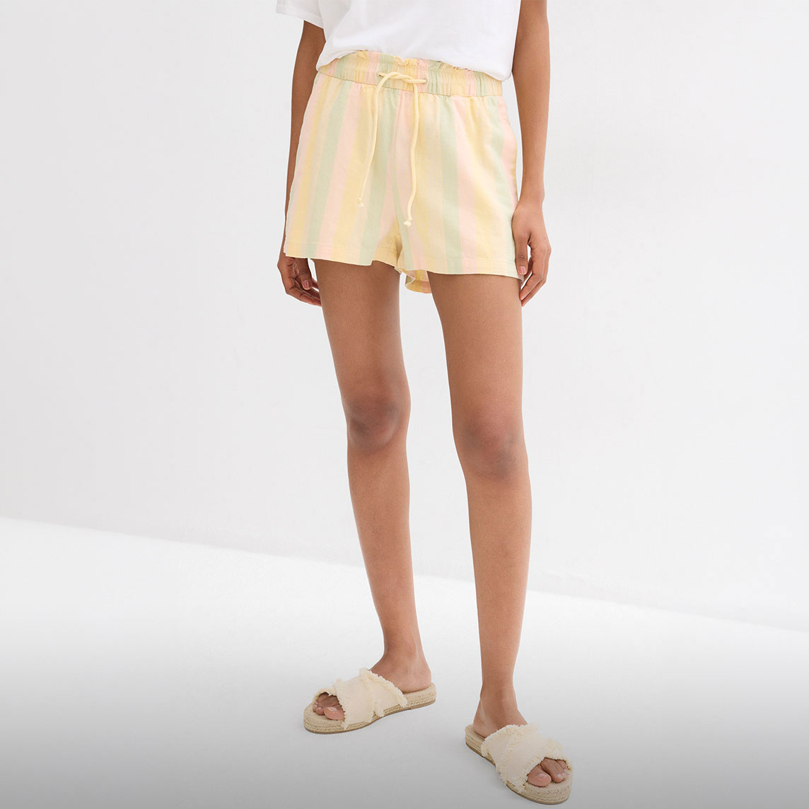 Gestreifte Pastell-Shorts, weißes T-Shirt und bequeme Bast-Sandalen für warme Tage.