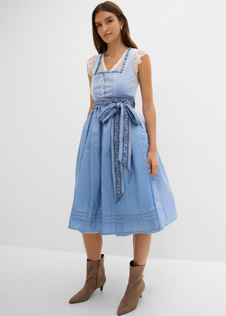 Ein hellblaues Dirndl mit Spitzenbluse, floralem Schürzenband und braunen Stiefeletten.