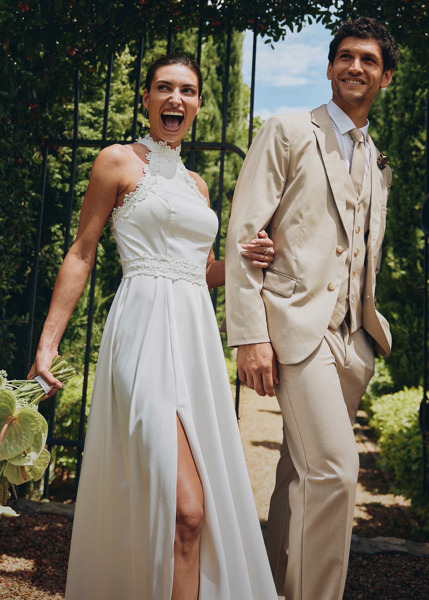 Elegantes weißes Hochzeitskleid mit Spitze und Schlitz, beiger Anzug mit Weste für den Bräutigam.