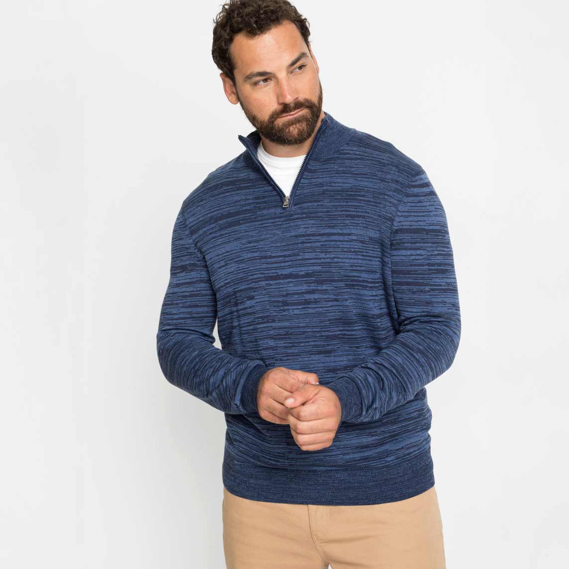 Blaumelierter Pullover über weißem T-Shirt, kombiniert mit beiger Hose. 