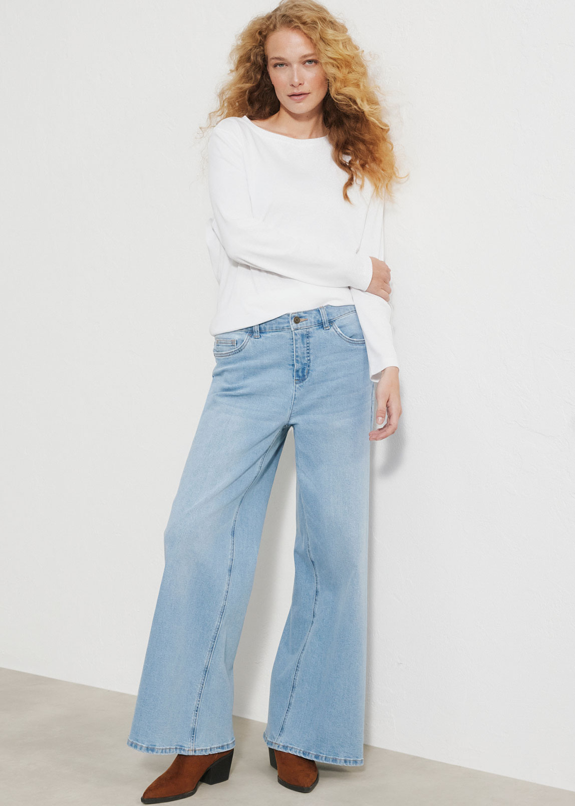 Ein weißes Langarmshirt, eine weite hellblaue Jeans und modische braune Stiefeletten.