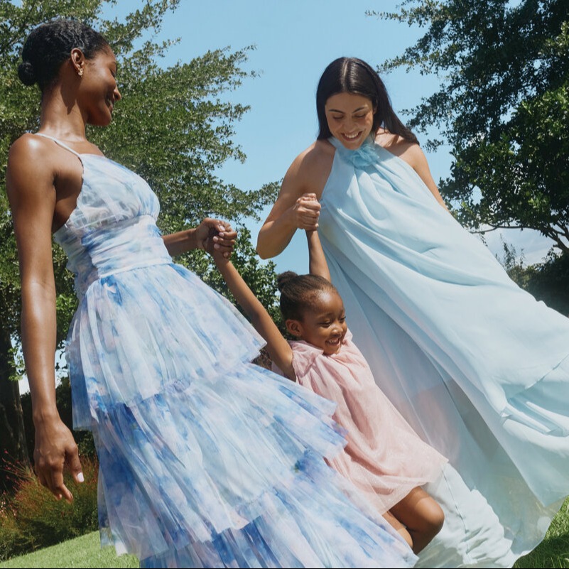 Zwei Frauen und ein Kind tragen elegante, luftige Sommerkleider in Pastelltönen.
