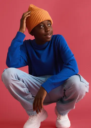 Orange Mütze, blauer Pullover, helle Jeans und weiße Turnschuhe.