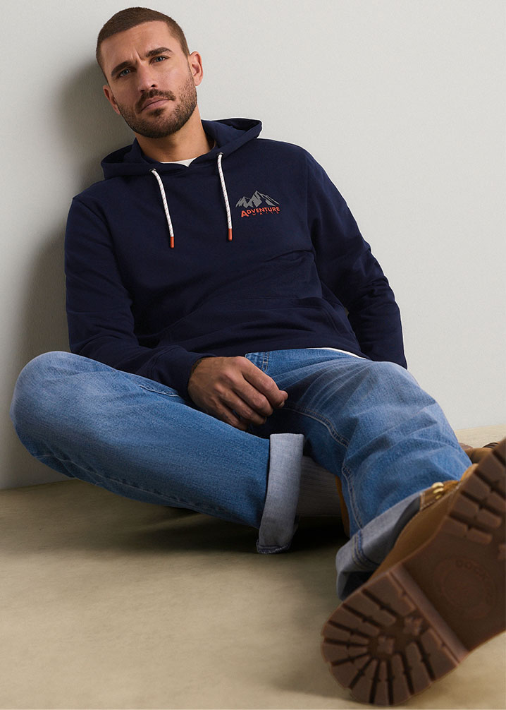 Ein modischer marineblauer Hoodie mit Bergmotiv, dazu blaue Jeans und robuste braune Stiefel.