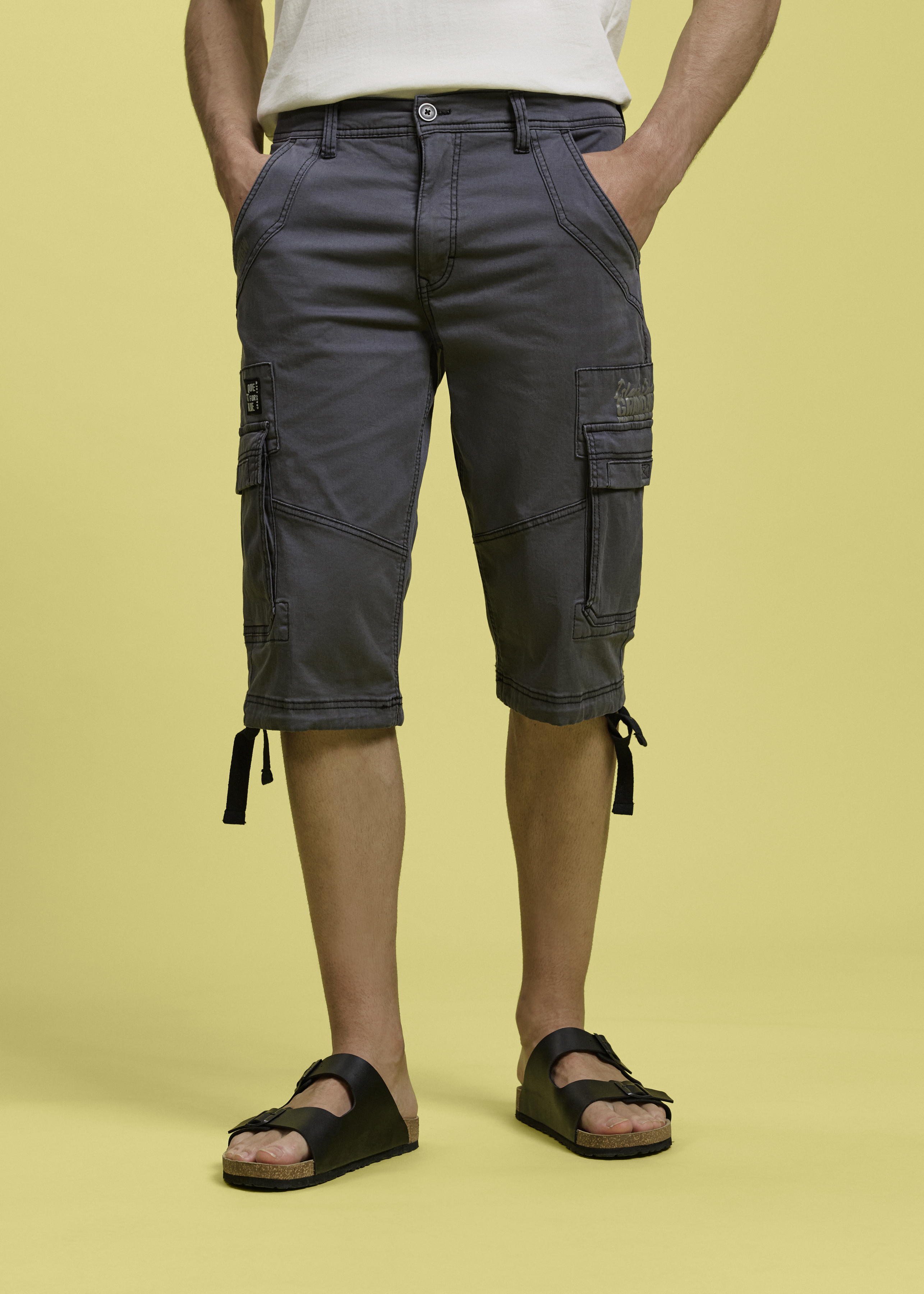 Graue Cargo-Shorts mit praktischen Seitentaschen, weißes T-Shirt und schwarze Sandalen.
